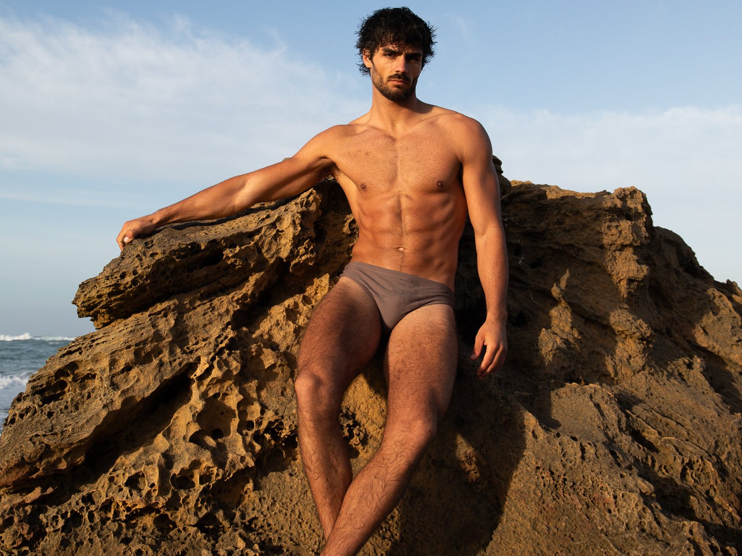Man standing on a rock wearing brown swim briefs