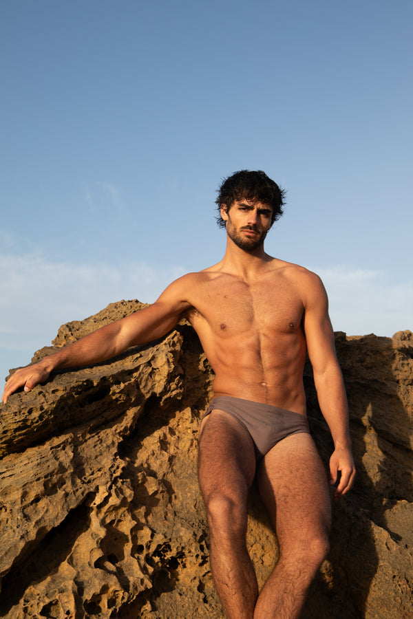 Man in a swimsuit sitting on rocks with a clear blue sky