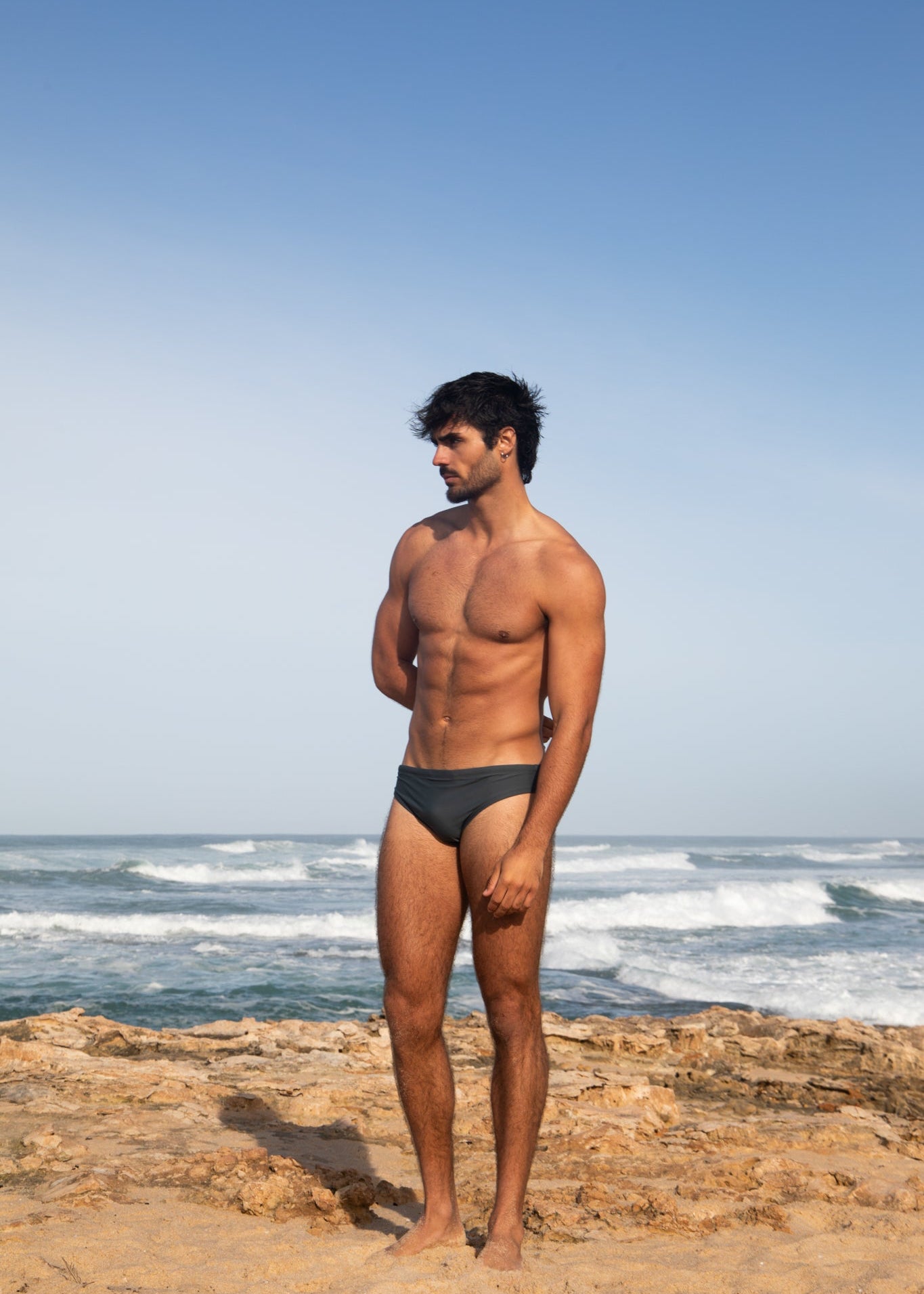 Man standing on a rocky beach with ocean waves and clear sky