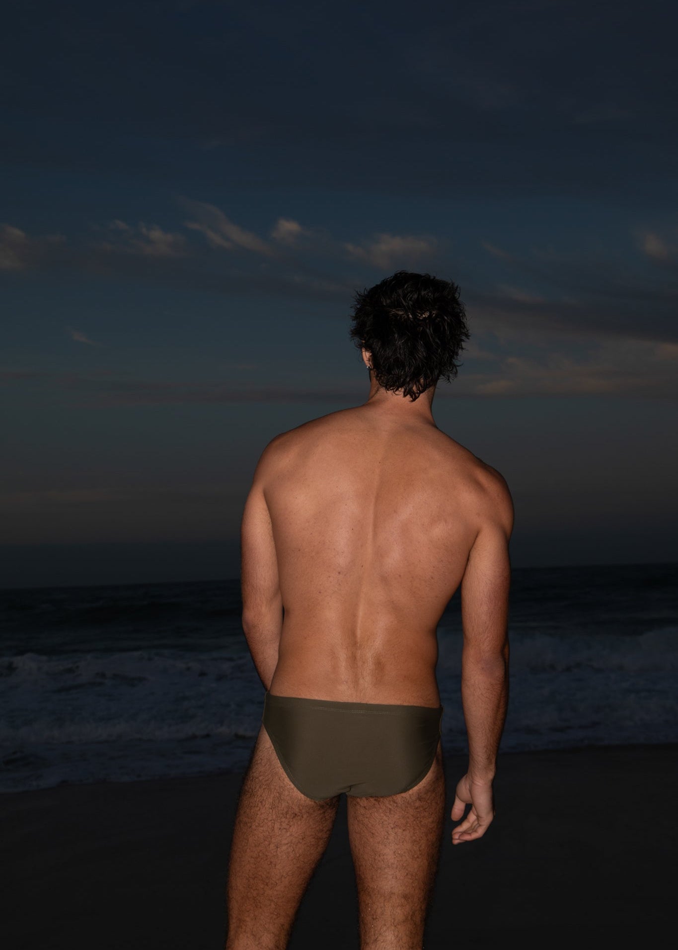 Man standing on a beach at night with dark sky and ocean.