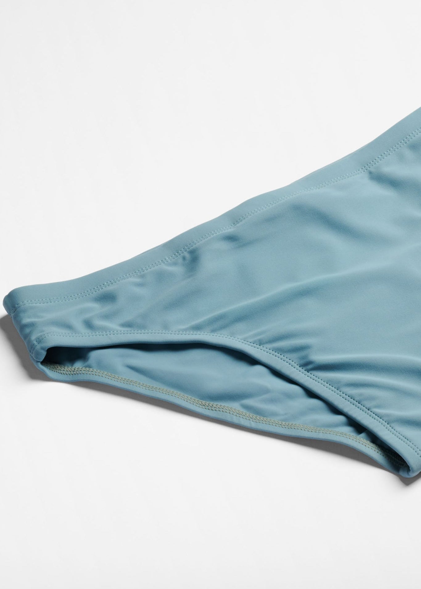 Close-up of a blue green swim briefs on a light gray background